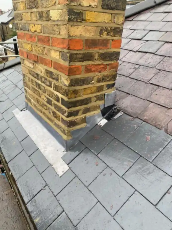 Lead apron flashing dressed around the base of a yellow brick chimney on a slate roof