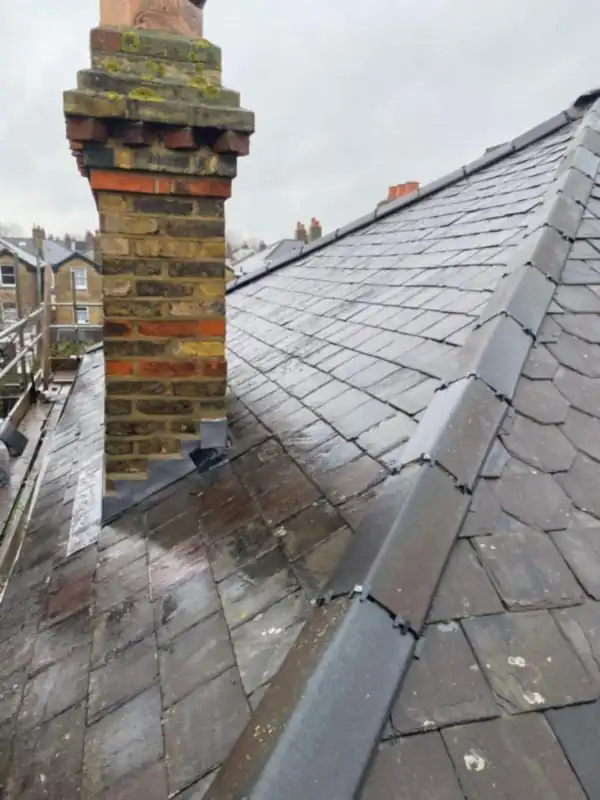 Brick chimney stack with new lead flashings beside the ridge of a grey slate roof