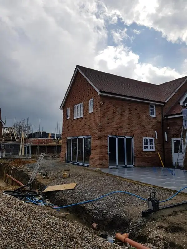 New-build brick house with a tiled roof, bi-fold doors and a ladder against the wall