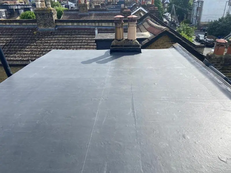 Black EPDM rubber flat roof laid around a chimney stack among terraced rooftops