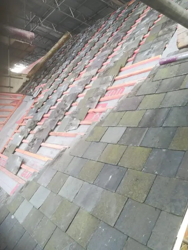 Old slates being stripped from a roof under a temporary scaffold roof, with new battens showing