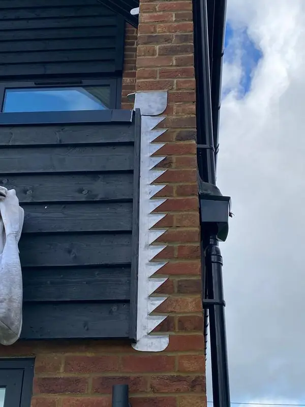 Stepped lead flashing where a brick wall meets black timber cladding beside a downpipe